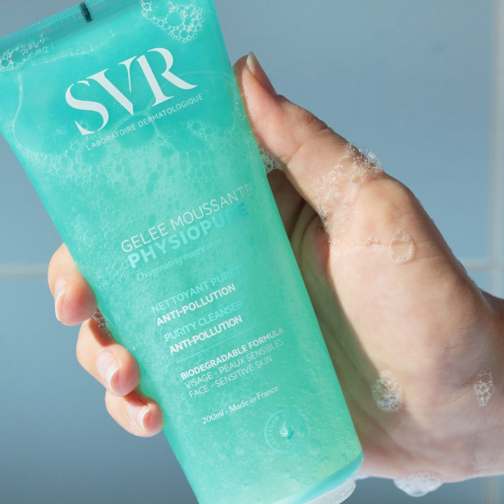 Main tenant un tube turquoise. Mousse sur la main. Sur le tube, Gelee Moussante Physiopure.