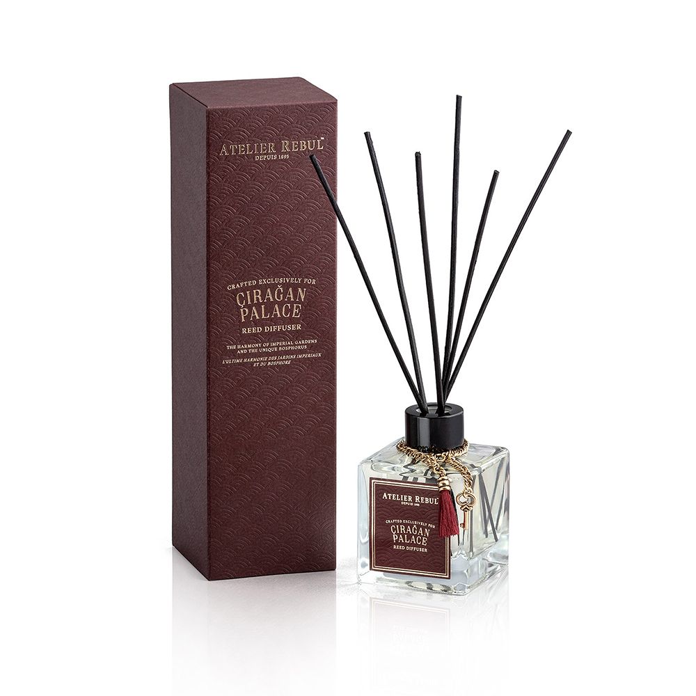 Schilfrohr-Diffusor mit Verpackung. Rechteckige Glasflasche mit schwarzen Stäbchen. Braune Verpackung mit Text.