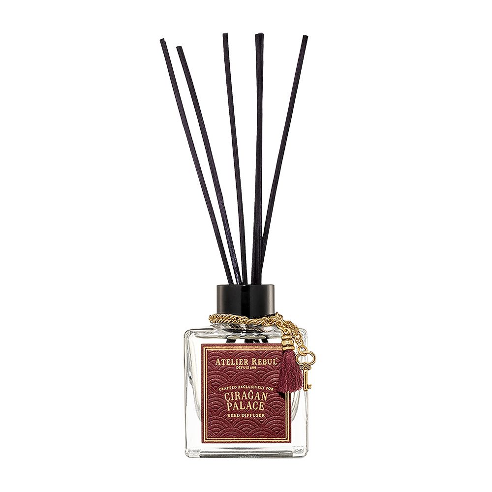 Schilfrohr-Diffusor. Rechteckige Glasflasche mit schwarzen Stäbchen. Goldene Kette und roter Quaste.