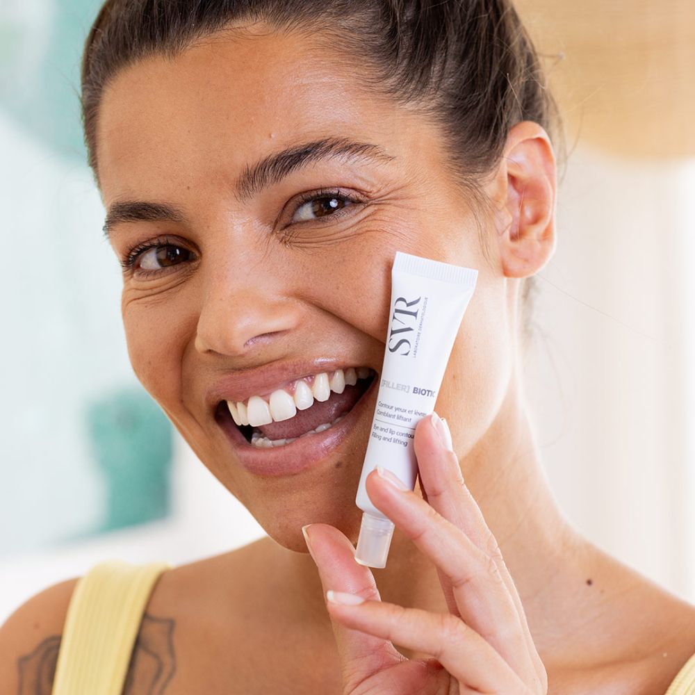 Femme tenant un tube. SVR [FILLER] BIOTIC, pour le contour des yeux et des lèvres. Femme souriante.