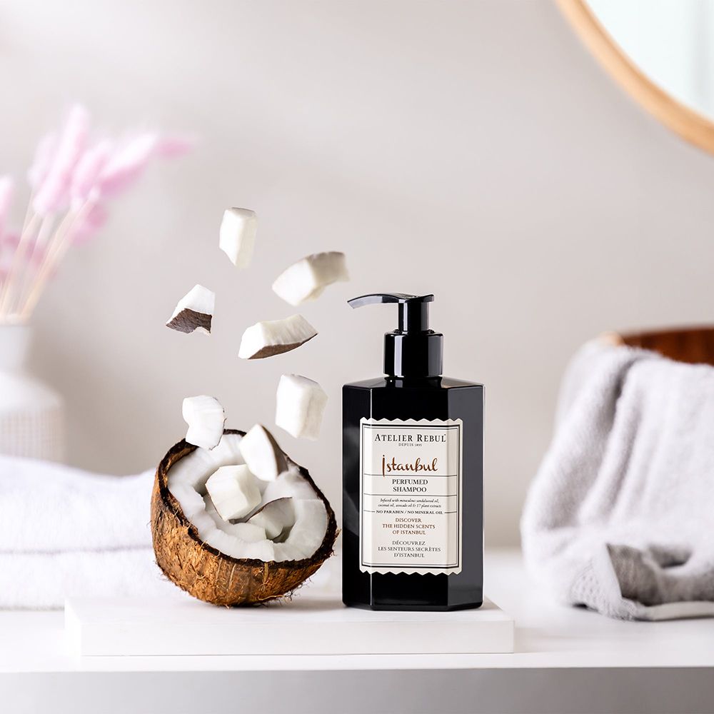 Schwarze Flasche mit Dosierpumpe, neben einer Kokosnuss und Kokosnussstücken. Produkt: Istanbul Perfumed Shampoo von ATELIER REBUL.