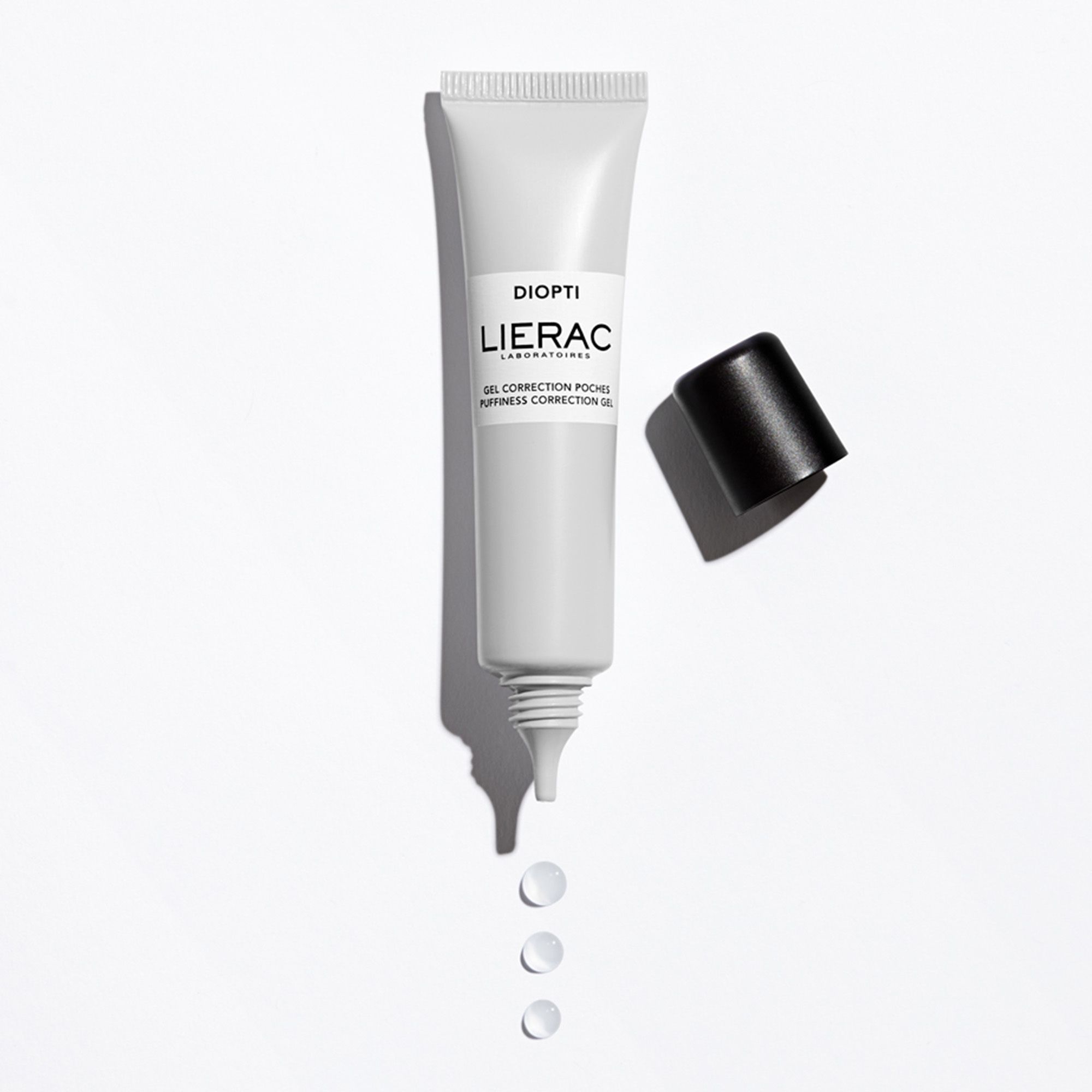 Tube blanc, bouchon noir à côté. Inscriptions: DIOPTI, LIERAC, GEL CORRECTION POCHES, PUFFINESS CORRECTION GEL. Trois gouttes de gel.