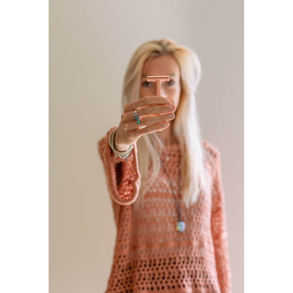 Vrouw houdt een koperkleurig T-vormig scheermes voor haar gezicht.