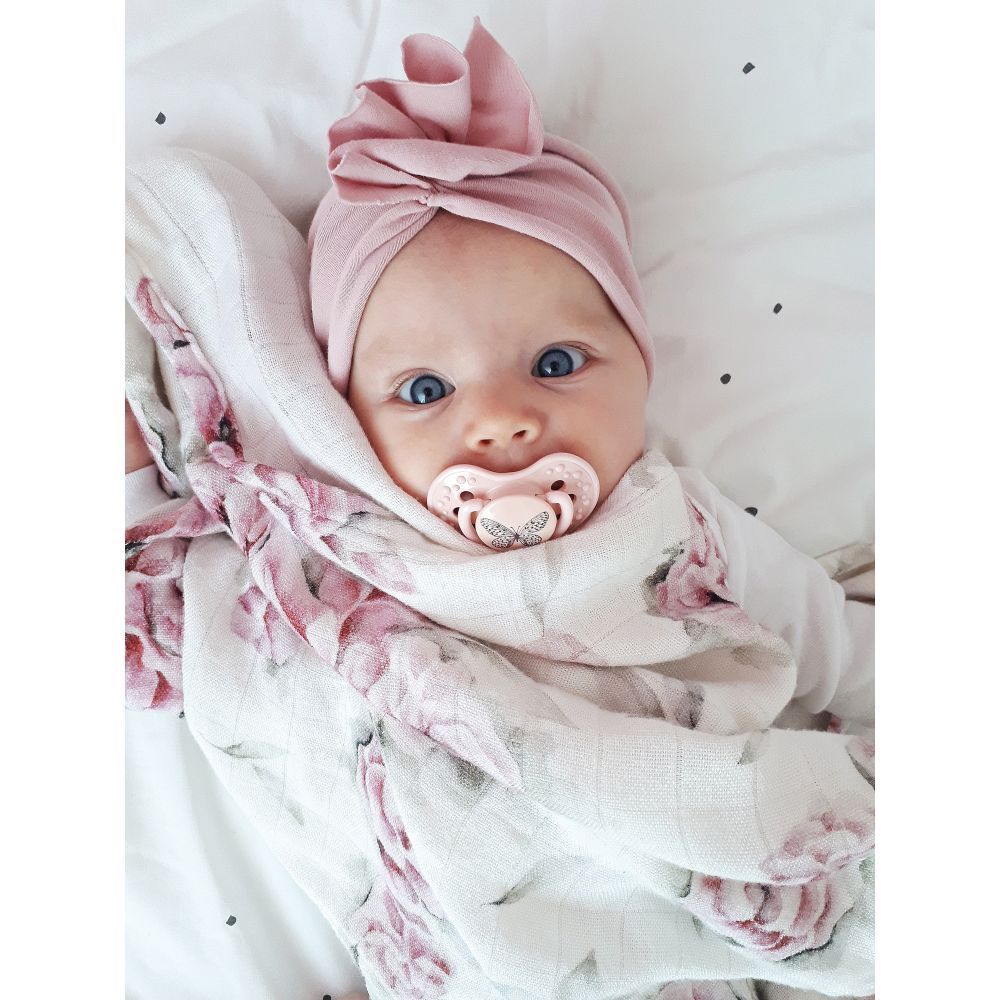 Bébé avec une sucette rose. Le bébé porte un turban rose et est enveloppé dans une couverture. Sucette avec papillon.
