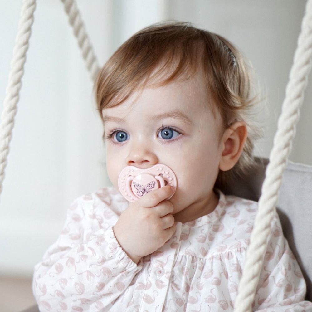Bébé avec une sucette rose dans la bouche. Bébé assis sur une balançoire.