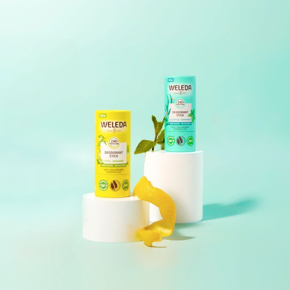 Deux emballages de déodorant stick sur socles. Jaune et vert menthe. Inscription: WELEDA, Déodorant Stick. Avec zeste de citron et branche.
