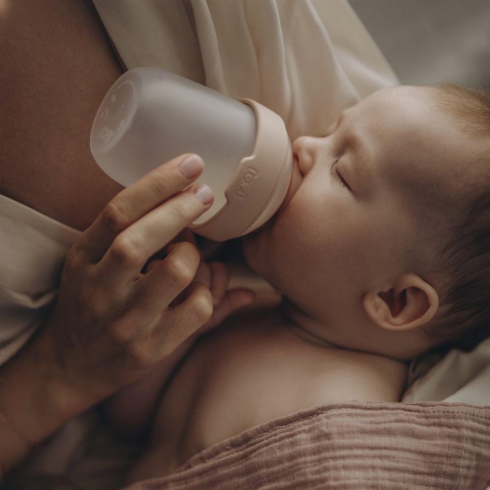 Baby trinkt aus einer Babyflasche. Person hält die Flasche.