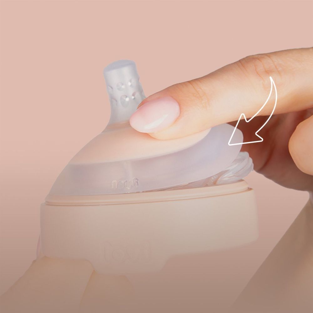 Hand hält Sauger. Rosa Basis, transparenter Aufsatz. Pfeil zeigt auf die Basis.