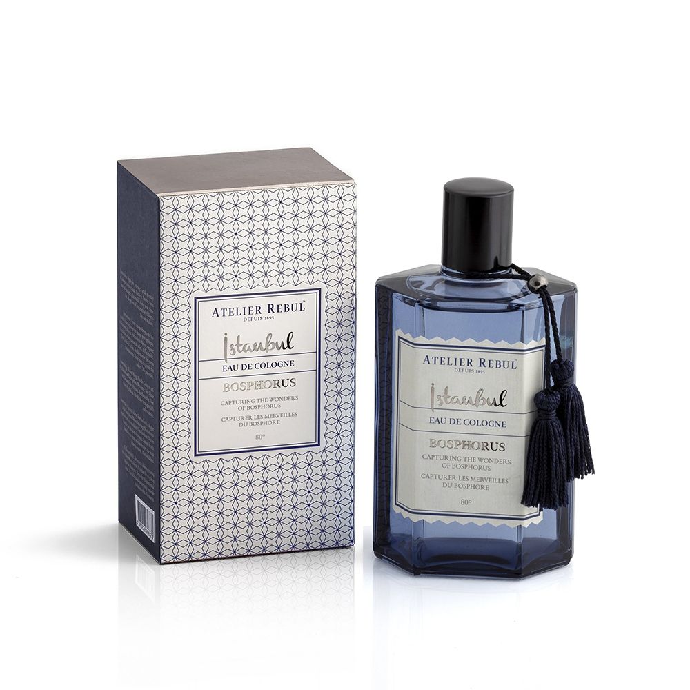 Flacon bleu d'eau de Cologne, bouchon noir, pompon. Boîte rectangulaire avec motif et étiquette. Atelier Rebul.