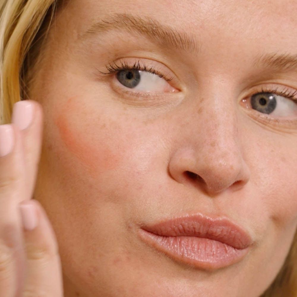 Gros plan d'une femme appliquant du blush sur sa joue.