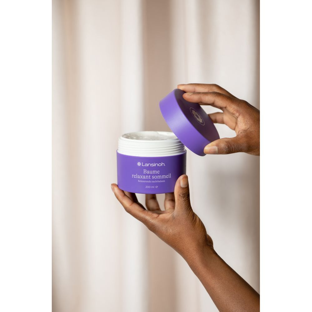 Mains ouvrant un pot violet. Produit blanc visible. Texte: Lansinoh, Baume relaxant sommeil, 200 ml.