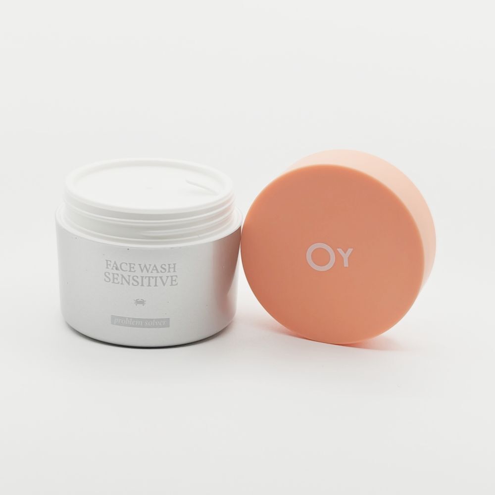 Pot de crème ouvert avec couvercle orange à côté. "FACE WASH SENSITIVE" est écrit sur le pot.