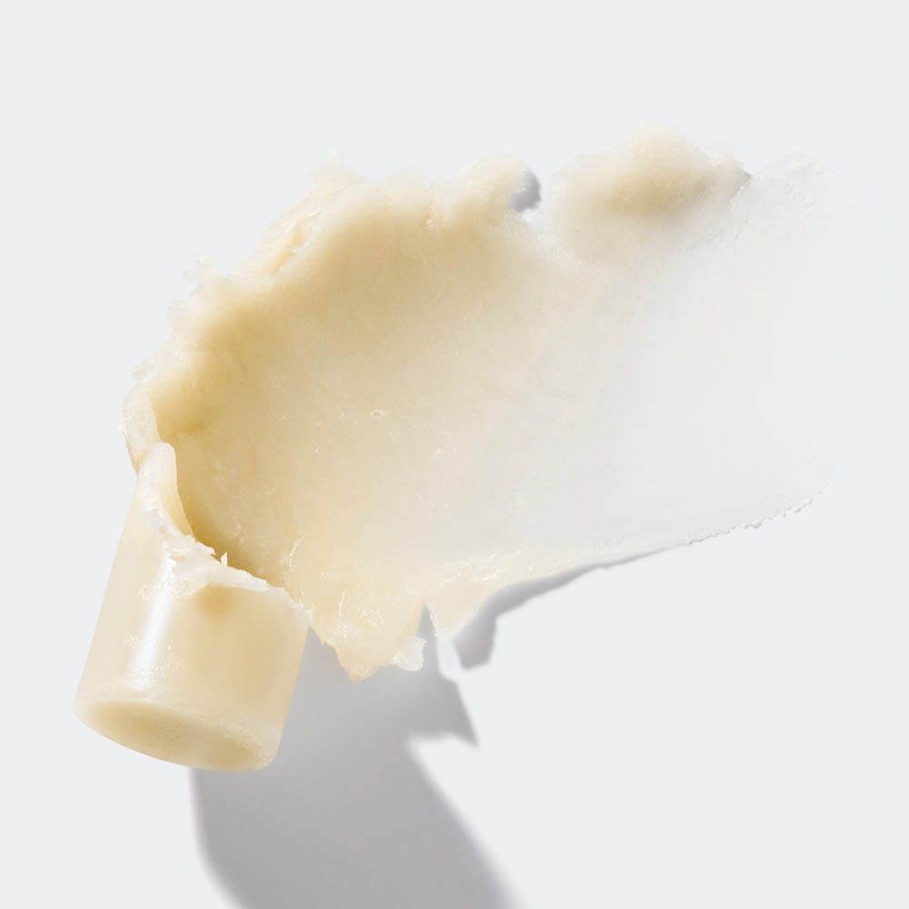 Texture crème sur fond blanc. Partie d'un contenant visible.