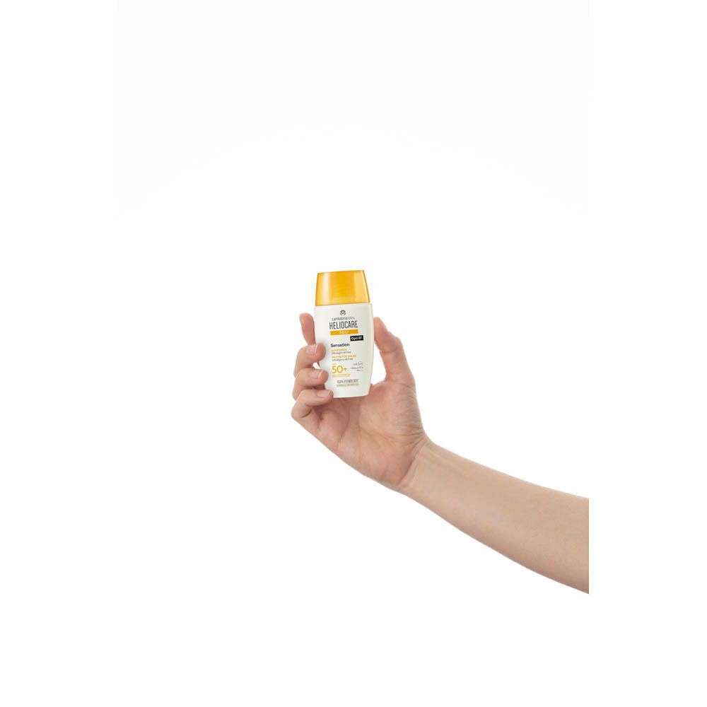 Main tenant un flacon Heliocare 360° Sensation SPF 50+. Blanc avec bouchon jaune. Texte : Heliocare, SPF 50+.