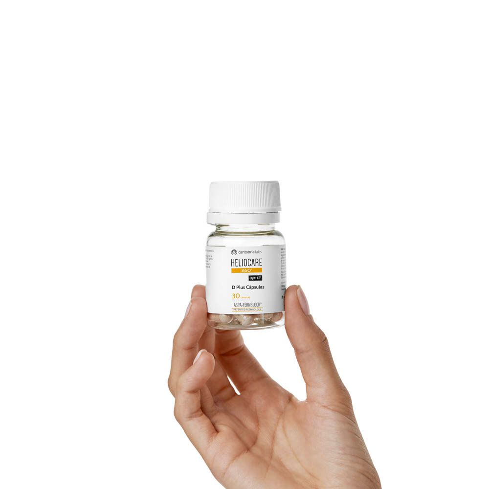 Hand die fles Heliocare 360° D Plus Capsules vasthoudt. Witte achtergrond.