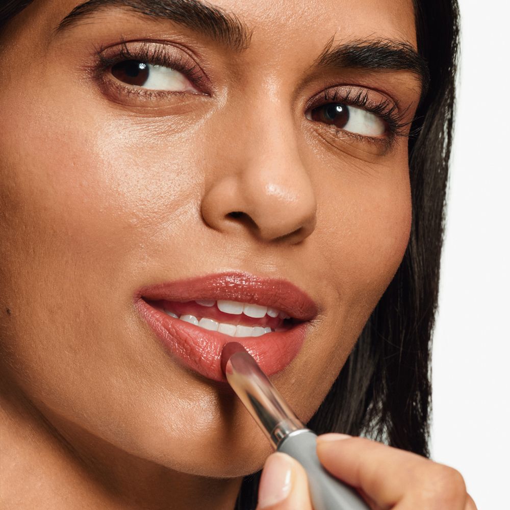 Frau trägt Lippenstift auf. Der Lippenstift ist rotbraun.