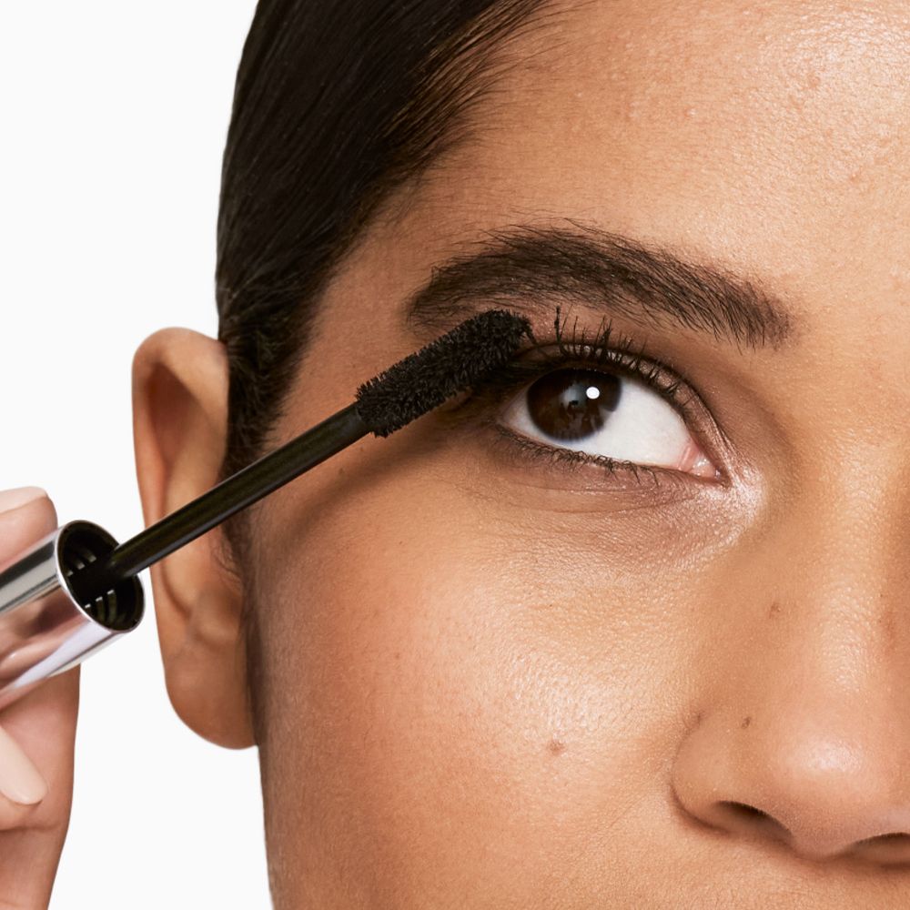 Frau trägt Mascara auf. Schwarze Bürste wird auf die Wimpern aufgetragen.