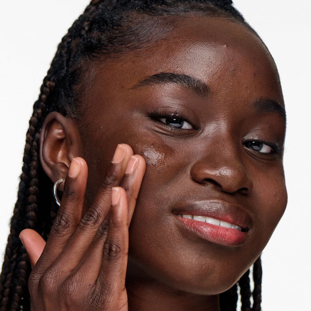 Dunkelhäutige Frau trägt Gel auf. Sie lächelt. Gel ist auf der Haut sichtbar.