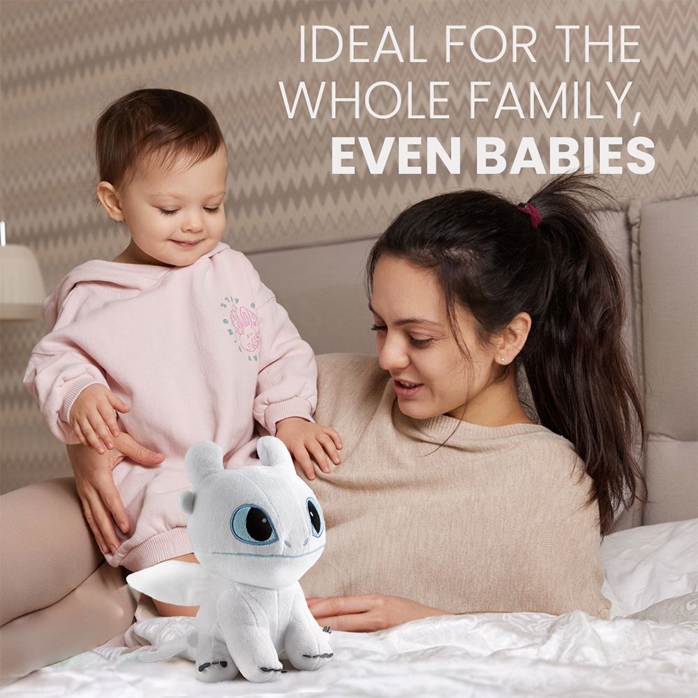 Frau mit Baby kuschelt mit weißem Plüschdrachen auf einem Bett.