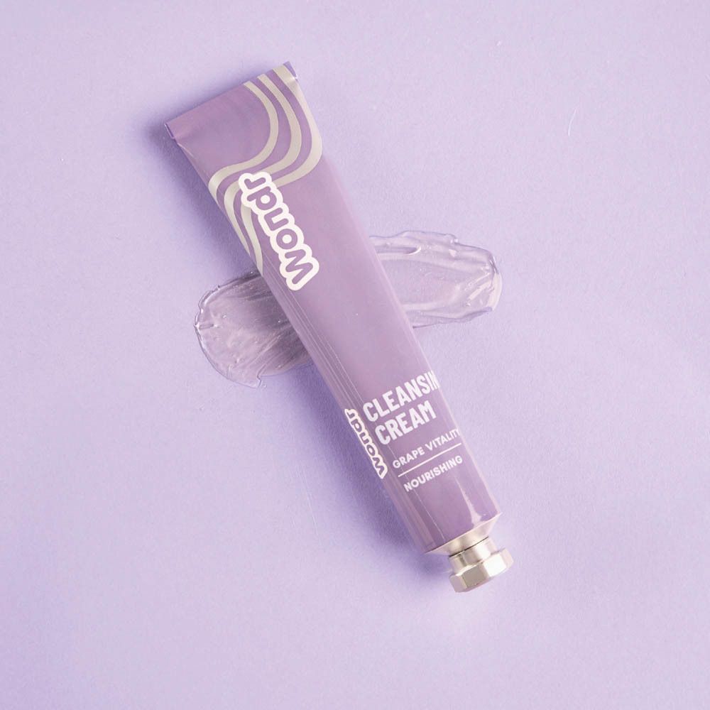 Paarse tube met "Wondr" logo en "Cleansing Cream Grape Vitality" tekst. Op paarse achtergrond met crèmevlek.