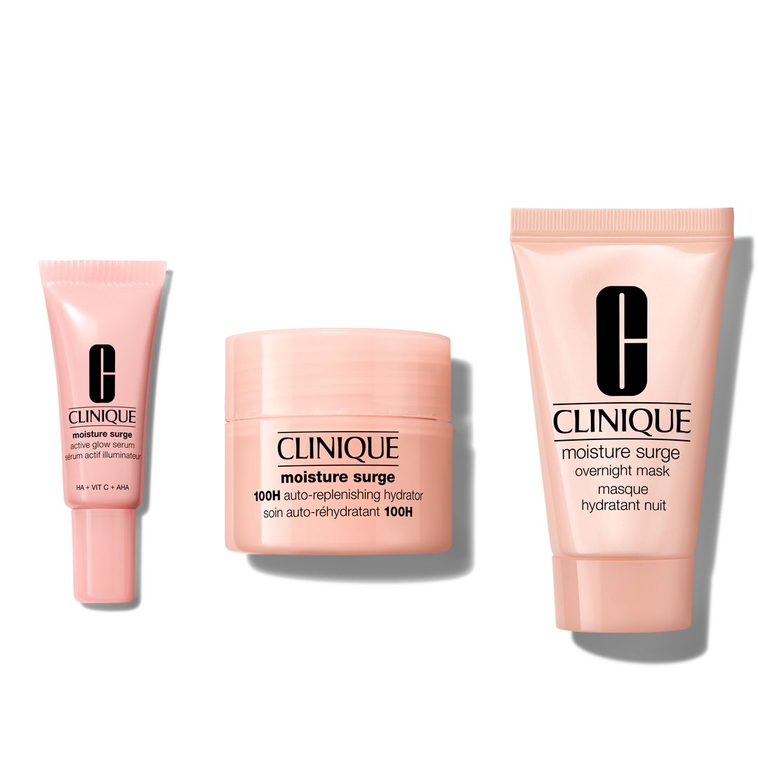 Drei Clinique Moisture Surge Produkte: Serum, Creme und Maske. Rosa Tuben und Tiegel mit schwarzem Logo.