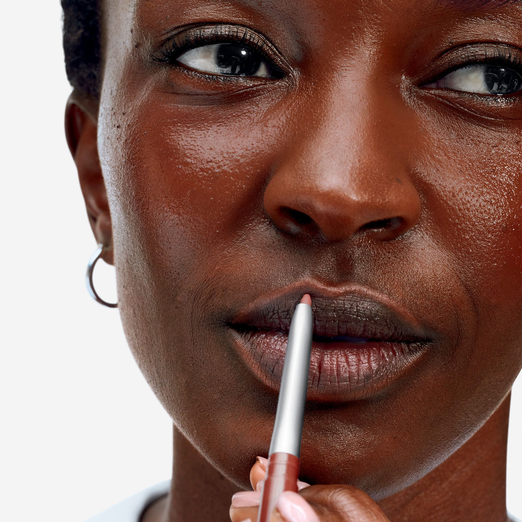 Nahaufnahme einer Frau, die ihre Lippen mit einem braunen Lipliner umrandet. Der Lipliner ist von Clinique.