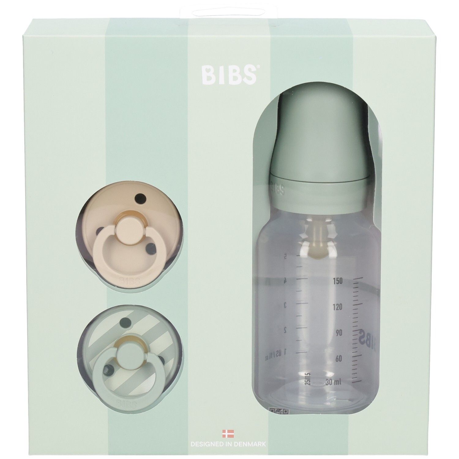 Geschenkset mit zwei Schnullern und einer Babyflasche in einer Schachtel. Die Flasche hat eine Messskala.