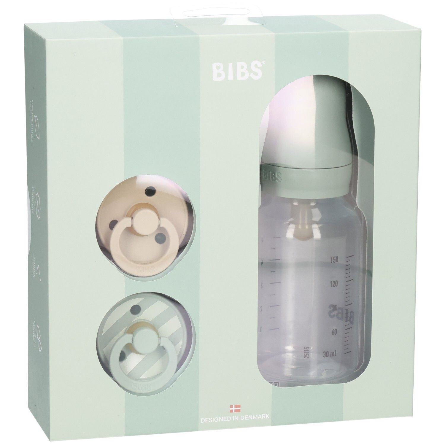 Geschenkset mit zwei Schnullern und einer Babyflasche in einer Schachtel. Die Flasche hat eine Messskala.