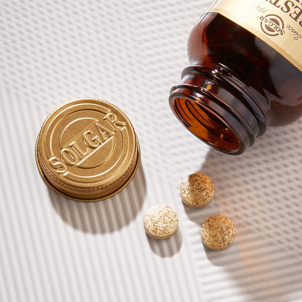 Braune Flasche und goldfarbener Deckel neben drei Tabletten. Tabletten sind beige und rund.