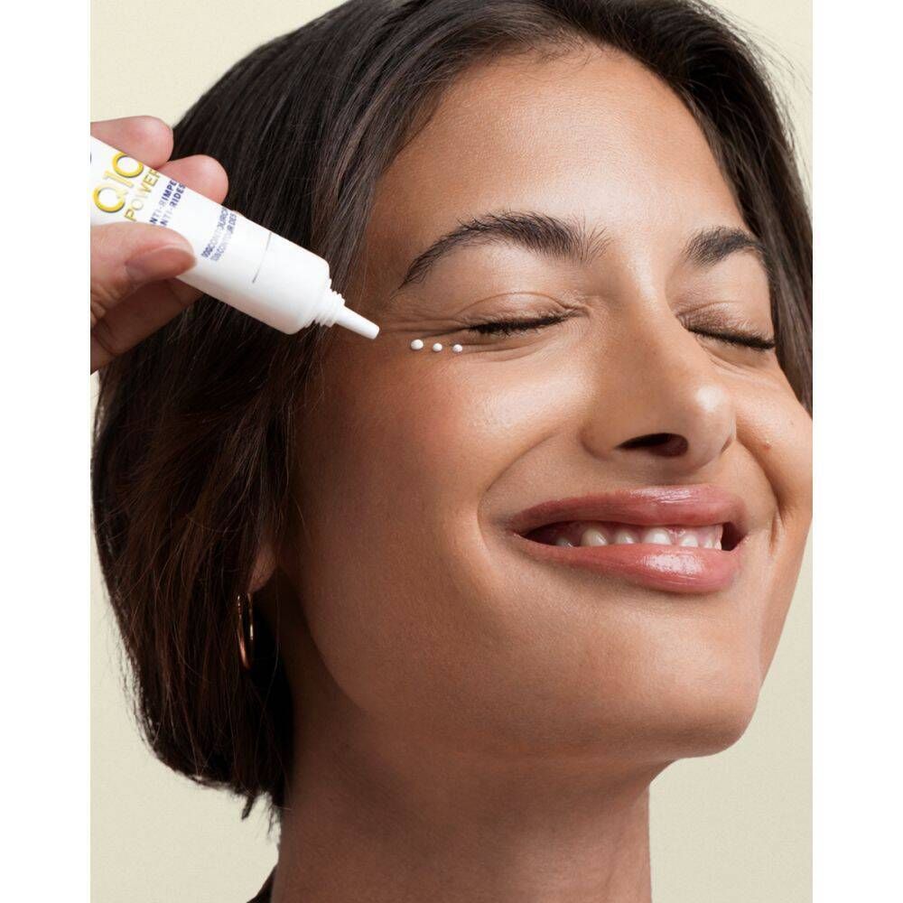 Femme aux yeux fermés. Une main tient un tube et applique de la crème. Produit : NIVEA Q10 Power Anti-rides pour le contour des yeux.