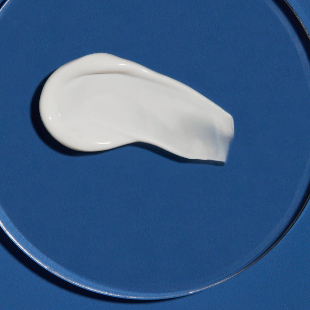 Weißes Sonnencreme-Produkt auf blauem Untergrund. Cremige Textur. Geformt wie ein breiter Tropfen.