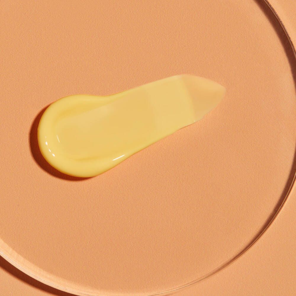 Gelbe Sonnenlotion auf orangefarbenem Untergrund. Creme-Textur, längliche Form. Auf einer transparenten Oberfläche.