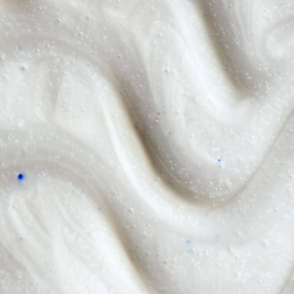 Nahaufnahme von weißer Creme mit blauen Partikeln. Cremige Textur mit Wirbeln.