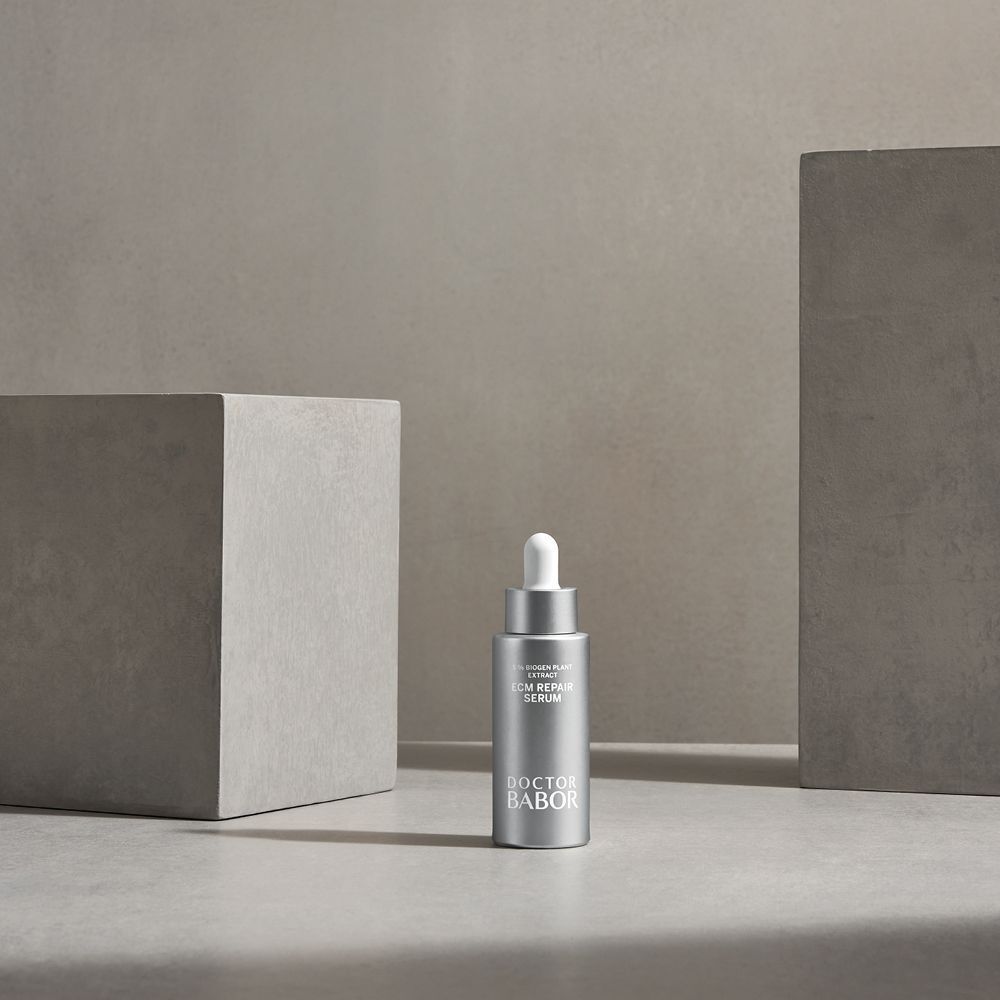 Silberne Flasche mit weißem Applikator. Beschriftung: ECM Repair Serum, Doctor BABOR. Steht vor Betonblöcken.