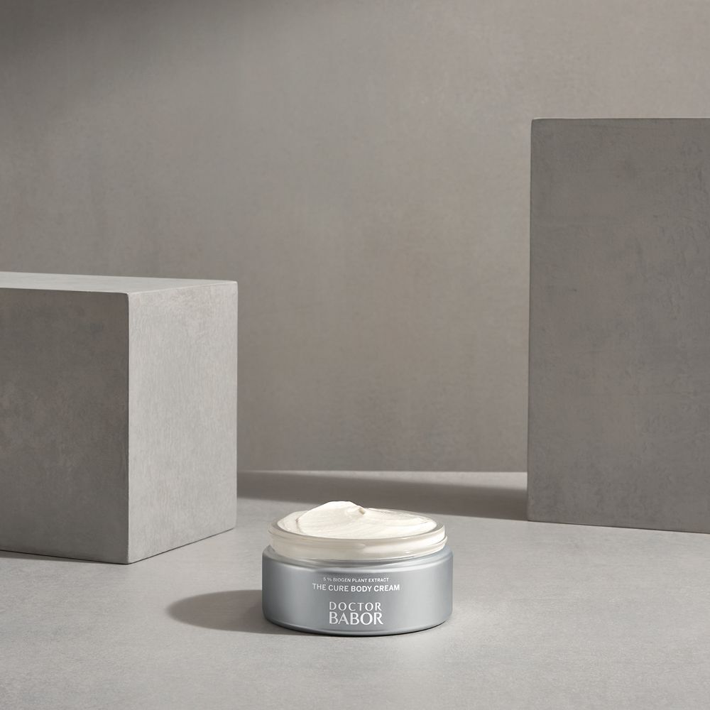 Pot argenté avec crème sur table. Inscription : THE CURE BODY CREAM, DOCTOR BABOR.