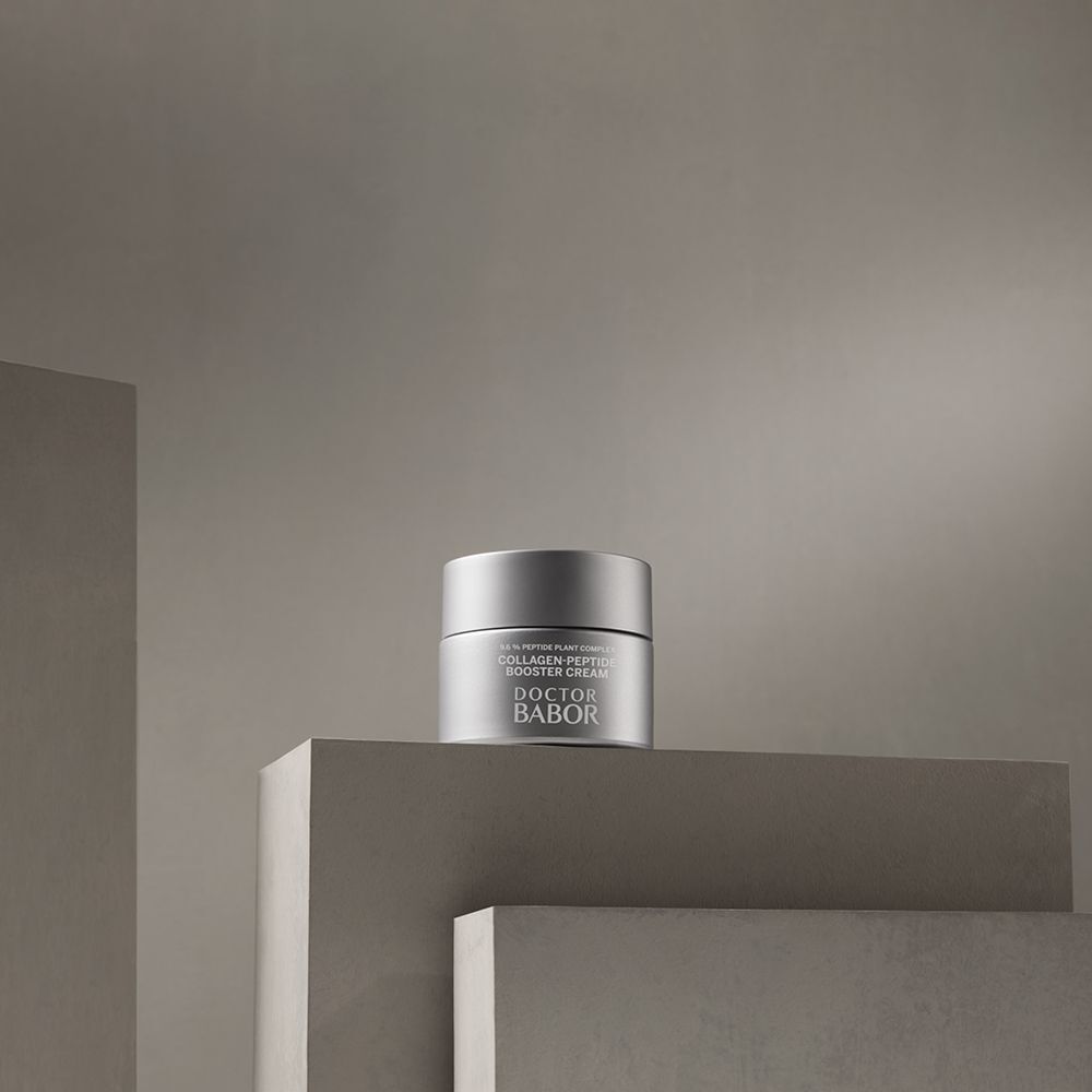 Pot argenté sur une surface. Inscription : Collagen-Peptide Booster Cream, Doctor BABOR.
