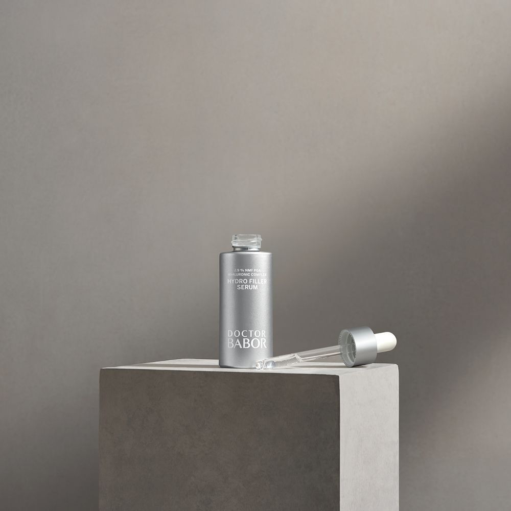 Silberne Flasche mit Tropfer auf Würfel. Aufschrift: Hydro Filler Serum, Doctor BABOR.