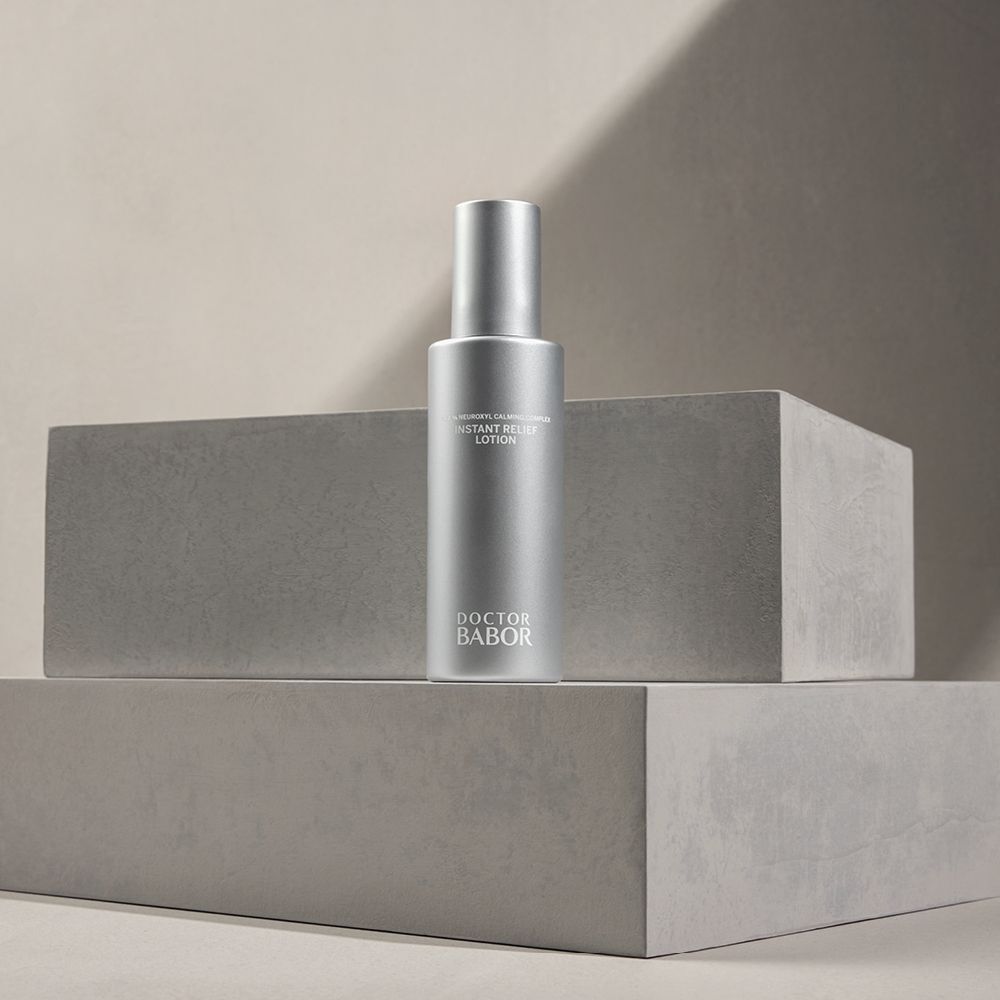 Silberne Lotion-Flasche auf grauen Blöcken. Aufschrift: Instant Relief Lotion, Doctor BABOR.