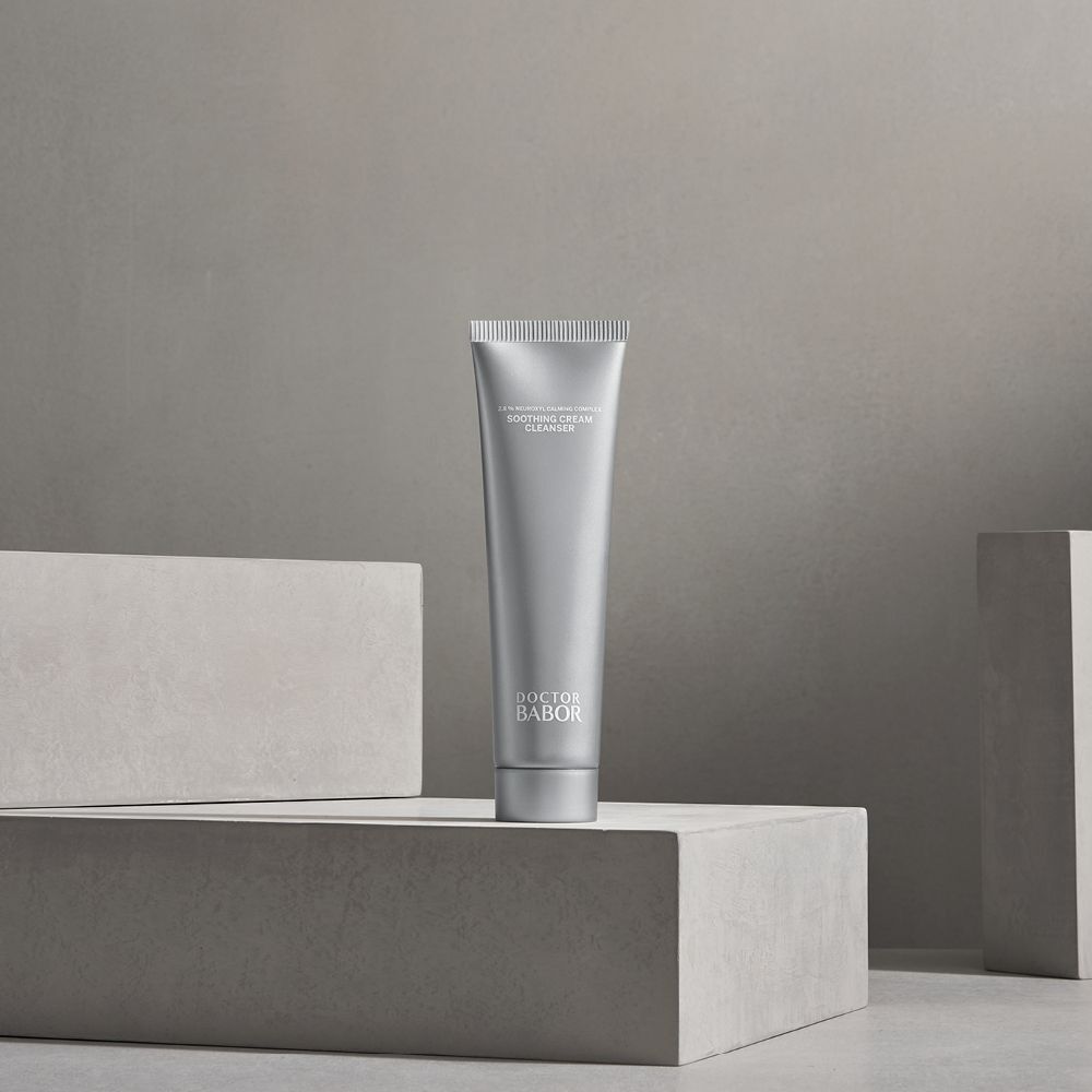 Silberne Tube "DOCTOR BABOR Soothing Cream Cleanser" auf grauen Blöcken. Produkt im Vordergrund.