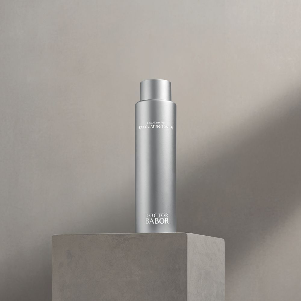 Flacon argenté avec bouchon à vis sur un socle gris. Inscription : Exfoliating Toner, Doctor BABOR.