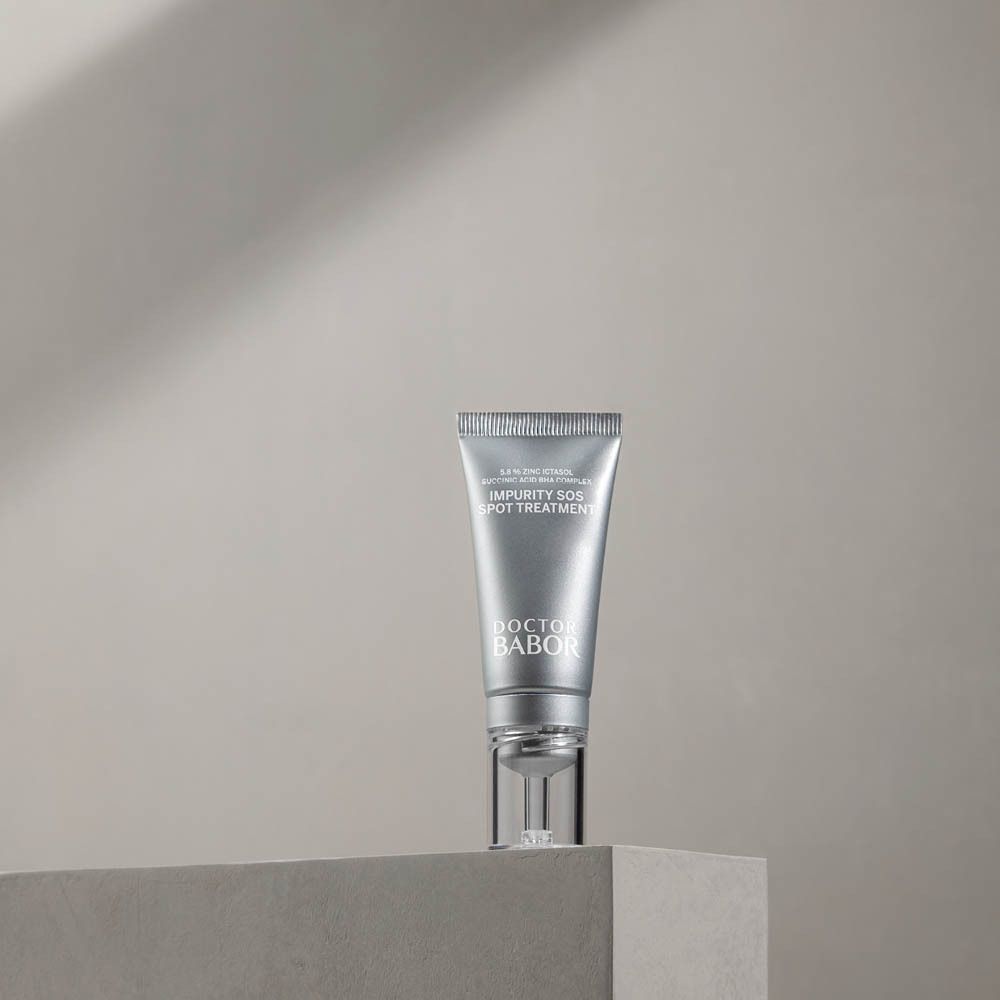 Silberne Tube mit transparentem Applikator auf einem Podest. Aufschrift: Impurity SOS Spot Treatment, Doctor Babor.