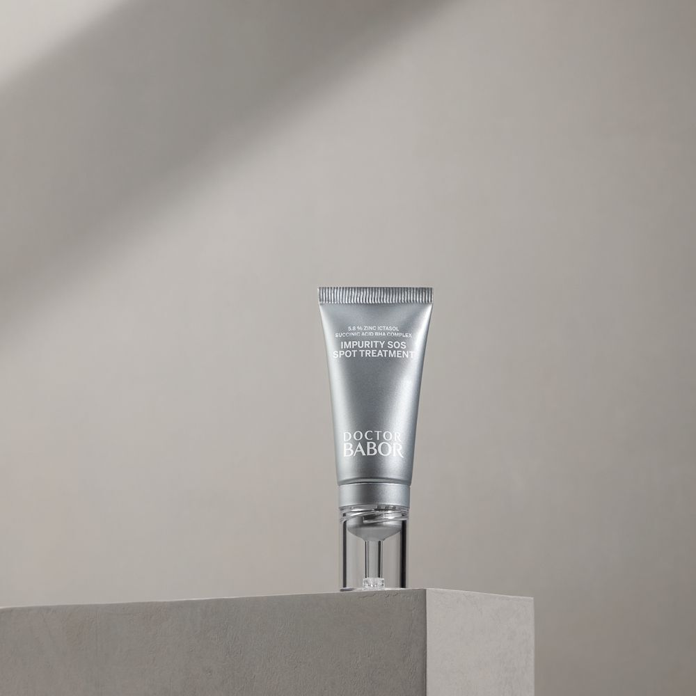 Tube argenté avec texte blanc. Nom du produit: IMPURITY SOS SPOT TREATMENT. Marque: DOCTOR BABOR. Sur une surface grise.