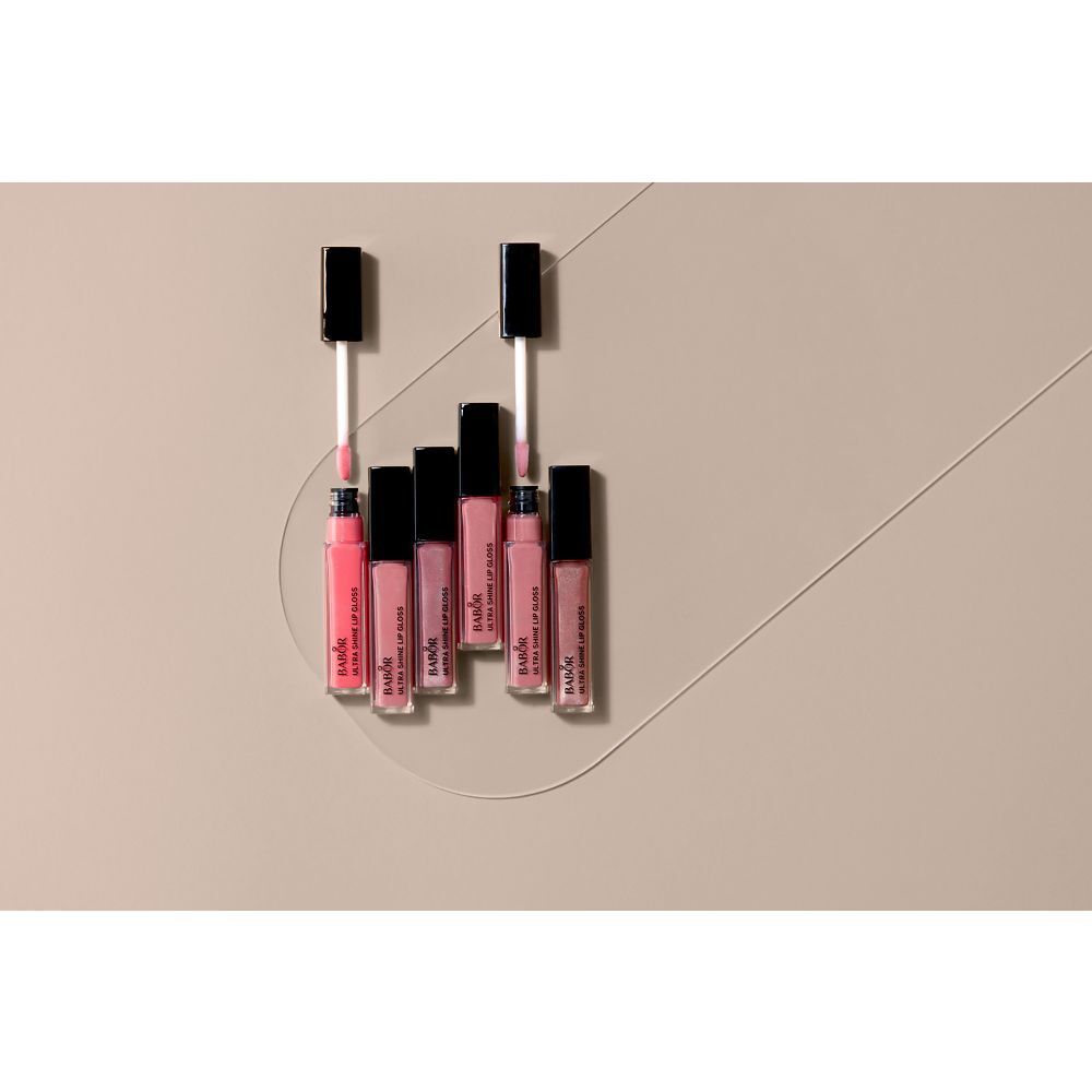 Mehrere Babor Ultra Shine Lip Gloss-Flakons. Rosa Farbtöne. Schwarze Deckel. Auf beigem Hintergrund angeordnet.