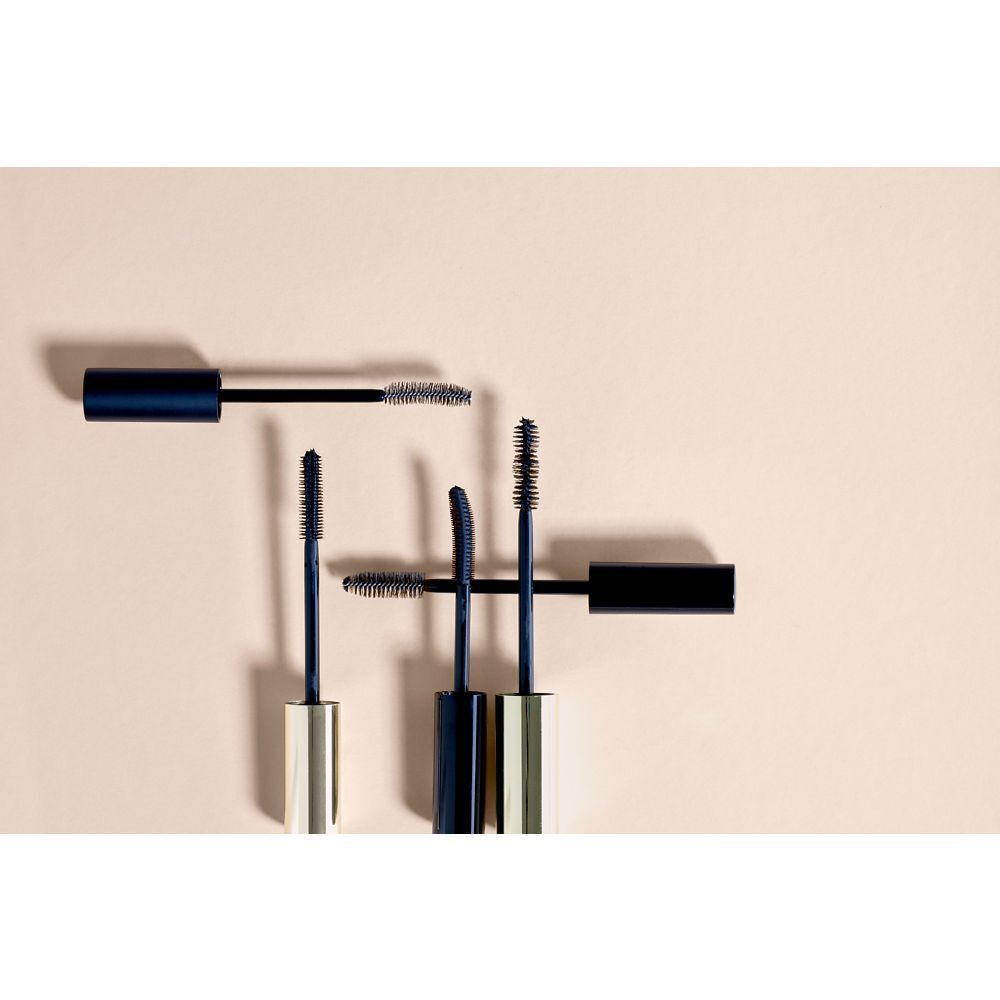 Mehrere Mascarabürsten in verschiedenen Winkeln. Schwarze und goldfarbene Elemente.