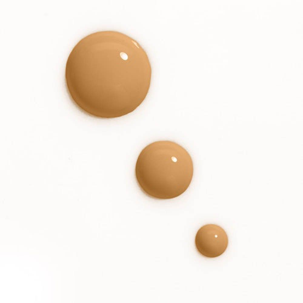 Drei Tropfen Foundation in verschiedenen Größen. Helle, beige Farbe. Auf weißem Hintergrund.