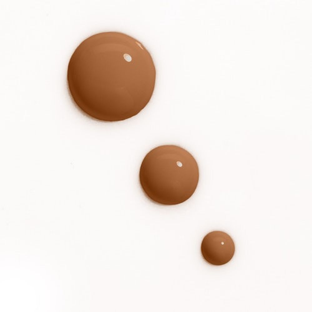 Trois gouttes de fond de teint de différentes tailles. Teintes marron clair sur fond blanc.