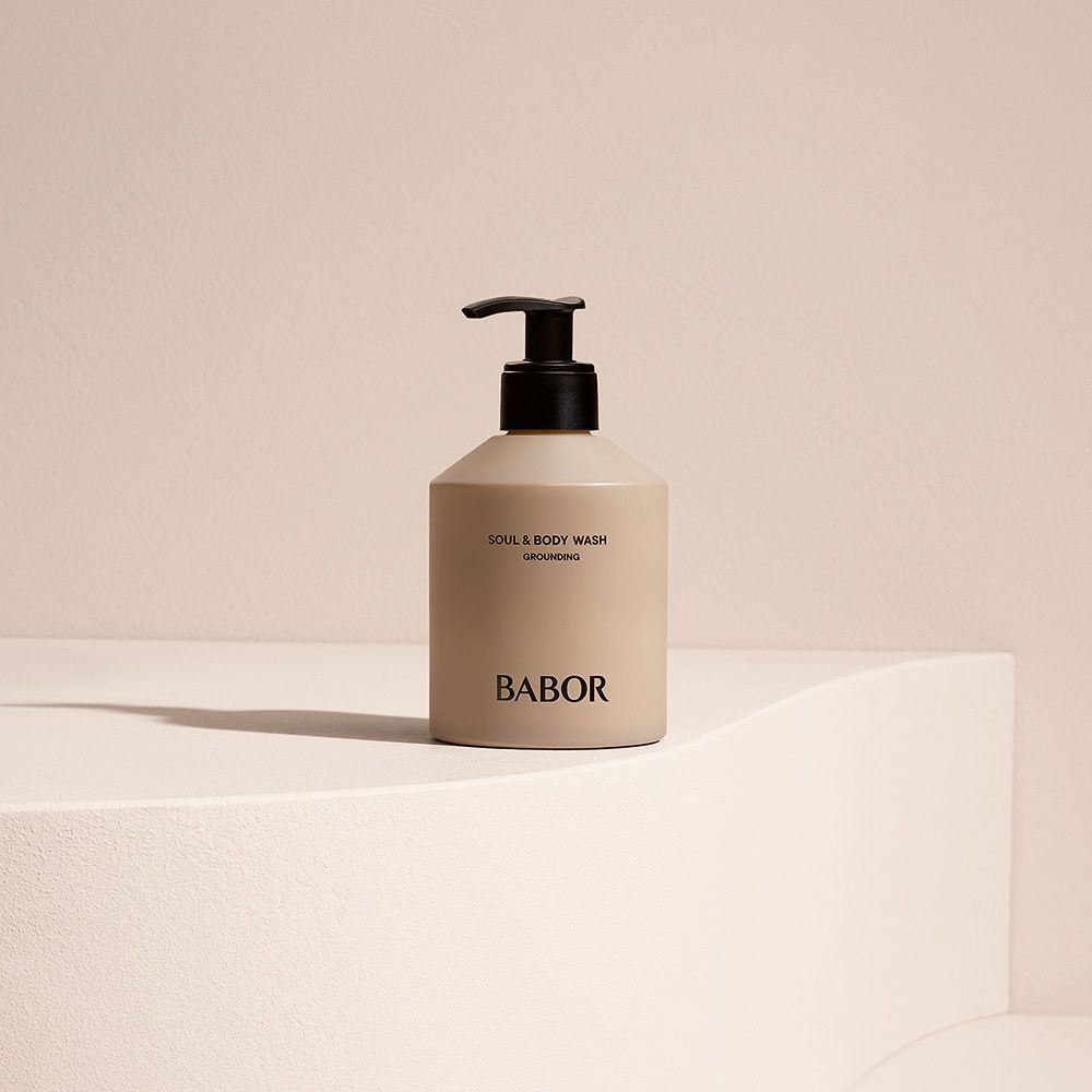 Flacon beige avec pompe noire sur socle blanc. Inscription : Soul & Body Wash, Babor.