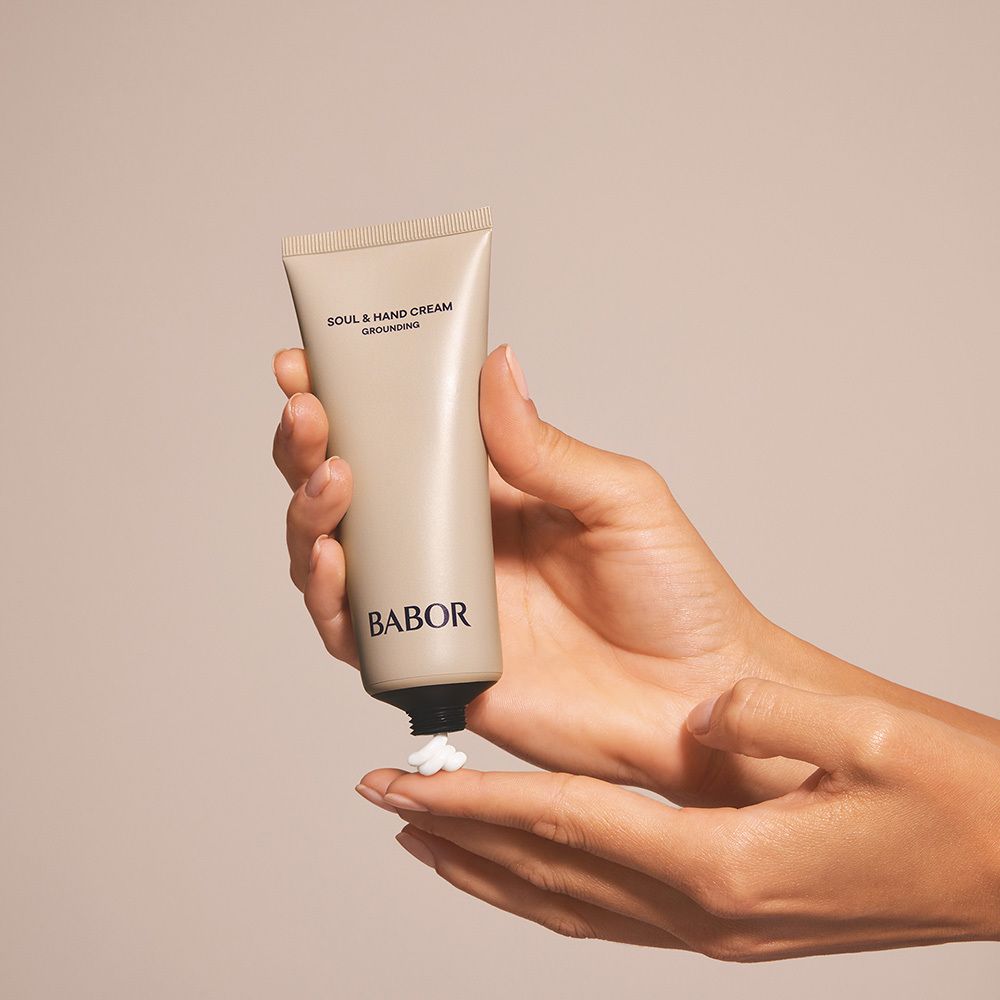 Hände halten eine Tube. Creme wird auf die Handfläche gedrückt. Aufschrift: SOUL & HAND CREAM GROUNDING. BABOR.