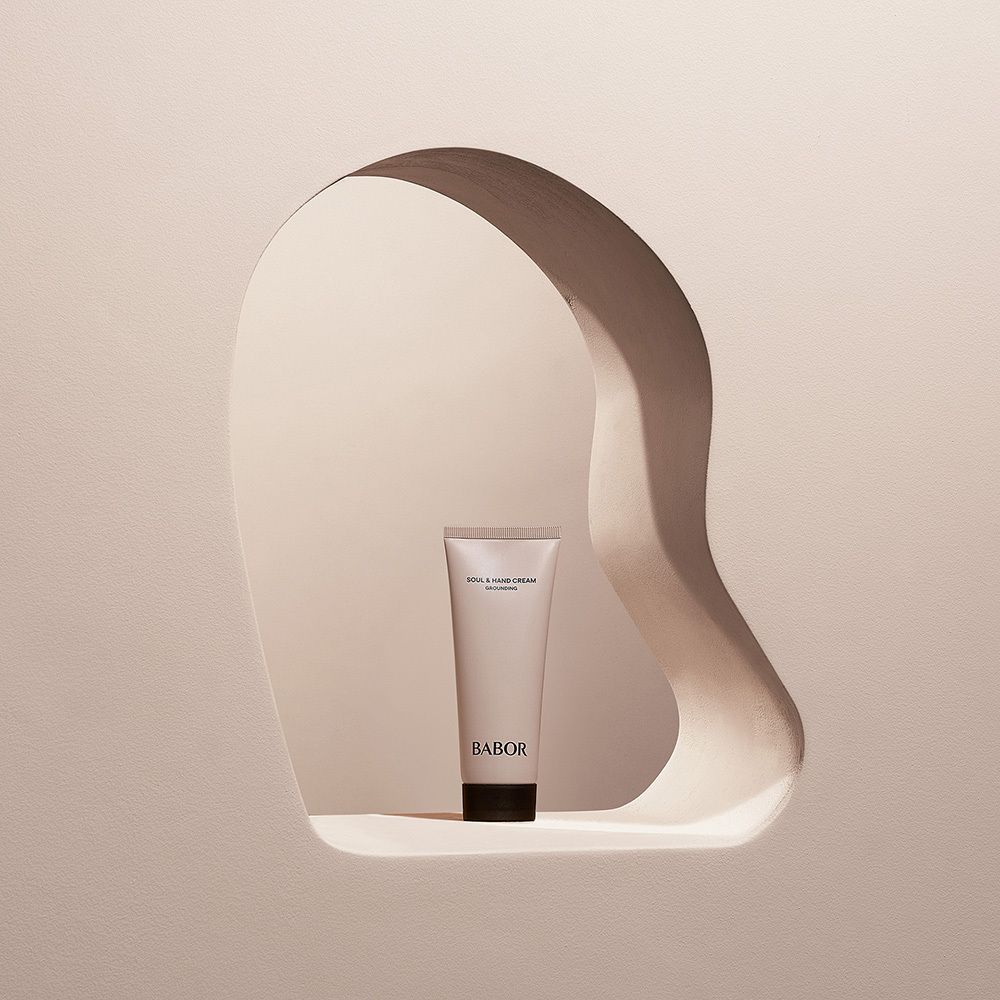 Beigefarbene Tube in einer Aussparung. Aufschrift: SOUL & HAND CREAM GROUNDING. Darunter BABOR.