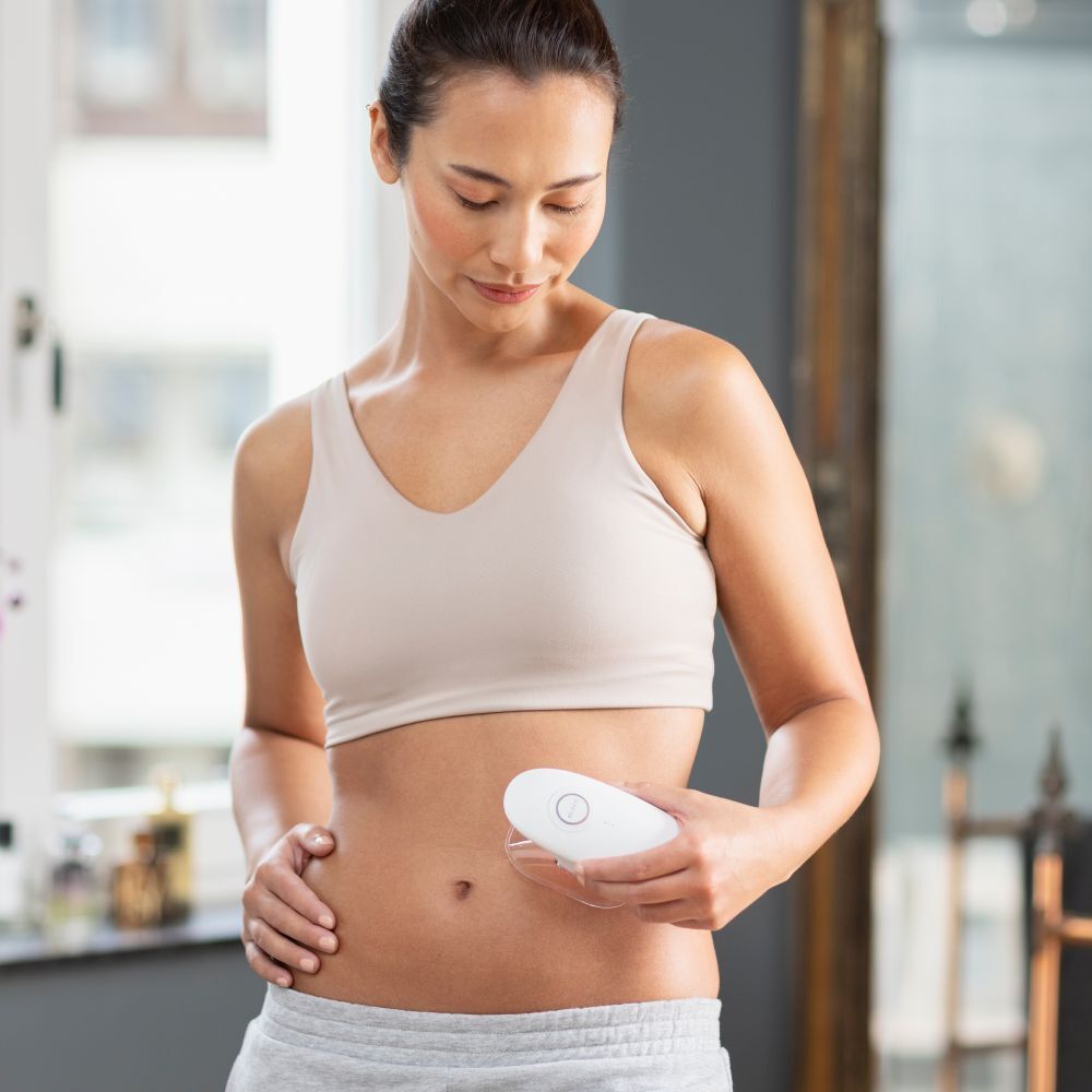 Vrouw houdt witte medisana VC 150 massager vast. Toepassing op buik. Draagt sport-bh en broek.